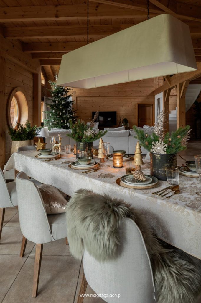 ubrany świąteczny stół w drewnianym domu, w głębi duży biały narożnik i choinka projekt Magda Gałach