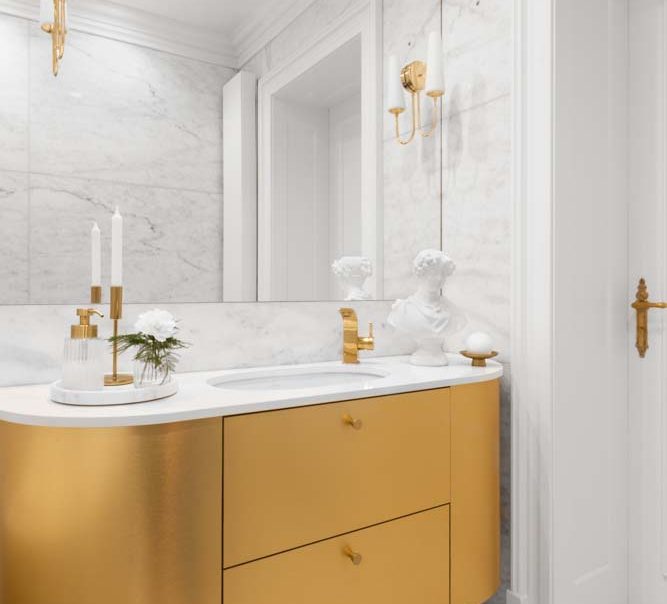 luksusowa biała marmurowa łazienka z dużym lustrem, ze złotymi kinkietami i złotą szafką projekt Magda Gałach