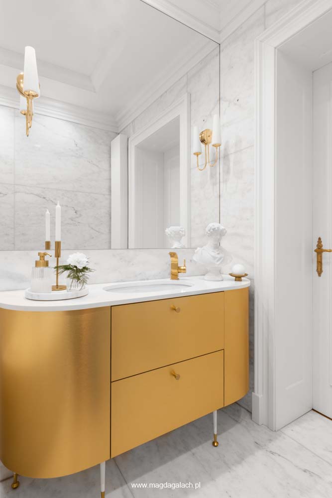 luksusowa biała marmurowa łazienka z dużym lustrem, ze złotymi kinkietami i złotą szafką projekt Magda Gałach