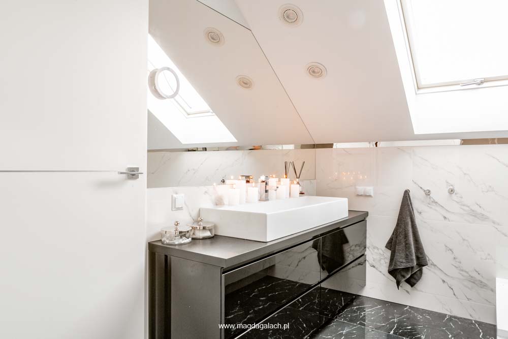 luksusowa łazienka pod skosem z białymi marmurowymi płytkami i czarną lakierowaną szafką