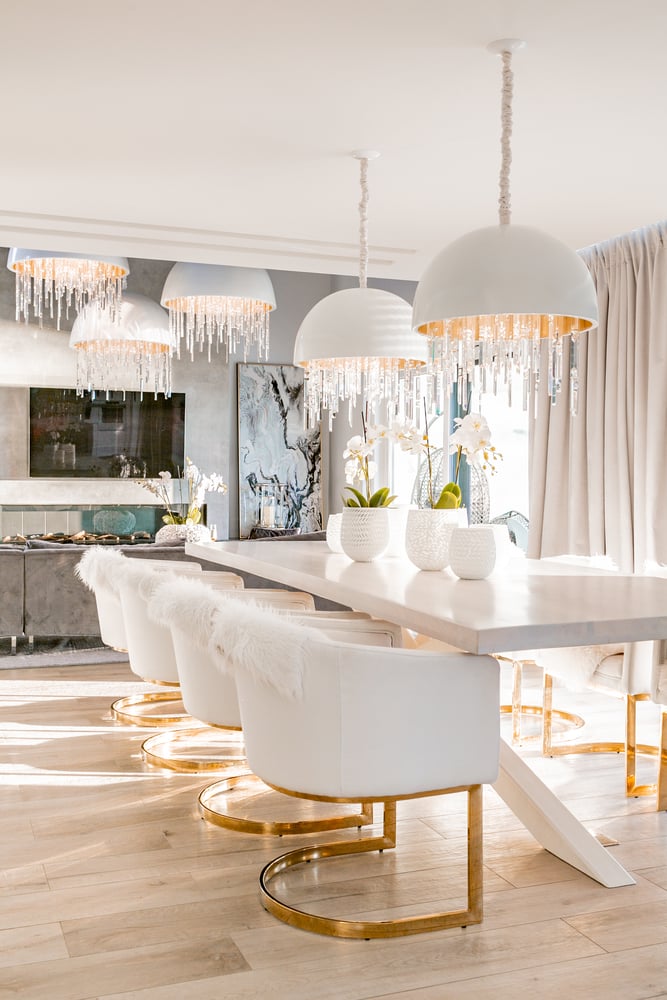 luksusowy salon z jadalnią z biało złotymi krzesłami i nowoczesnymi kryształowymi lampami oraz szarym narożnikiem
