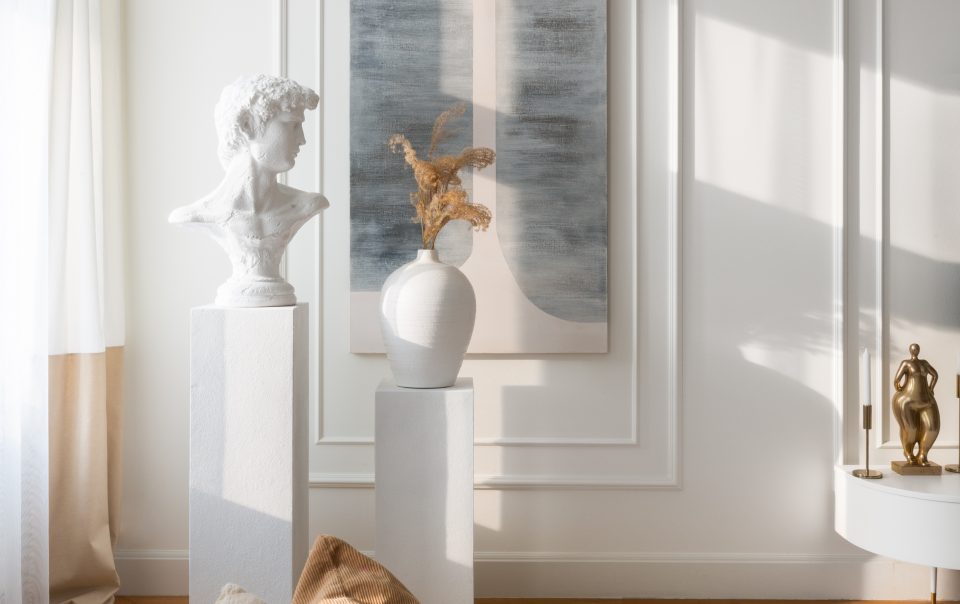 elegancki biały salon ze sztukaterią, rzeźbą i wazonem na postumencie oraz beżową aksamitną kanapa
